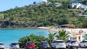 Un parking situé sur la côte, avec des voitures, une plage et des maisons sur une colline.