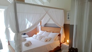 A bed with a canopy, white bedding, and a bedside table with a lamp. - Master suite + breakfast (saint martin)
