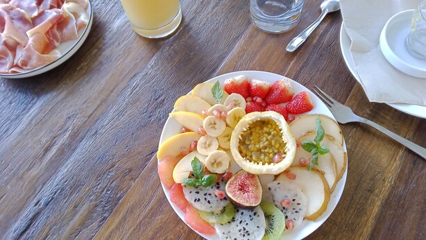 Une assiette de petit-déjeuner avec divers fruits et un verre de jus d’orange, posée sur une table en bois.