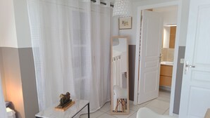 A modern living room with a white sofa, a small table with a decorative item, a white chair, and a large window with sheer curtains. - Master suite + breakfast (saint martin)