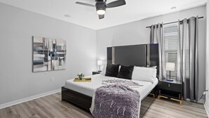 A modern bedroom with a bed, a ceiling fan, a TV, and a window with curtains.