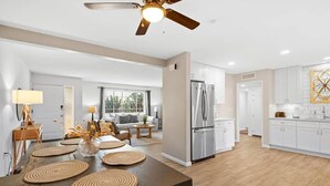 Una cocina moderna con un refrigerador de acero inoxidable, gabinetes blancos y una mesa de comedor de madera con individuales trenzados.