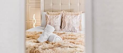 A neatly made bed with fluffy beige bedding and a white towel, a tufted headboard, and a decorative wall panel.