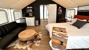 A tented accommodation with a bed, sofa, and round table.