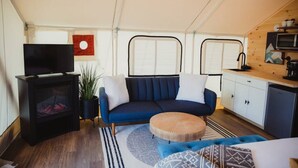 En kompakt opholdsstue med sofa, skammel, fjernsyn og tekøkken.