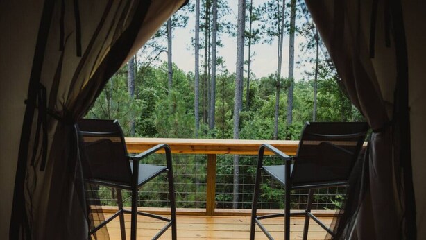 En balkon med to stole og gelænder i træ, med udsigt over et skovområde.