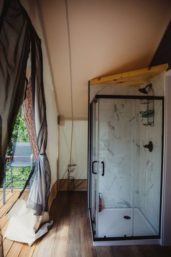 A glass-enclosed shower room with a wooden ceiling and a view of greenery outside.