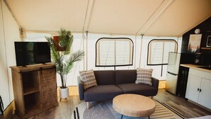 A cozy living area with a sofa, a coffee table, a TV on a wooden stand, and a potted plant. - The Chetopa, Luxury Safari Tent (Cadiz)