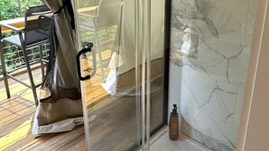 Une douche fermée par des parois de verre, avec un mur en marbre, une terrasse en bois à l’extérieur et une table avec des chaises.