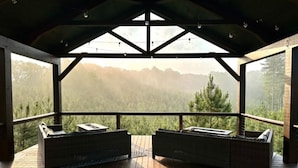 Un espace extérieur abrité, aménagé avec deux bancs rembourrés et une table, offrant une vue sur un paysage montagneux.