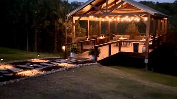 A wooden gazebo with a covered patio area, outdoor seating, and string lights.