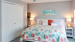 A bedroom with a bed, two bedside lamps, a ceiling fan, a white door, and a wall with a 'RELAX' sign. - Golden Tee in North Fort Myers (North Fort Myers)
