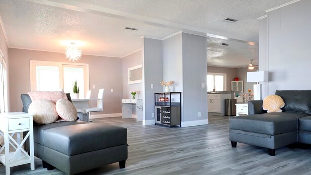 A modern living room with a grey sectional sofa, a white side table, and a dining area with a white table and chairs. - Golden Tee in North Fort Myers (North Fort Myers)
