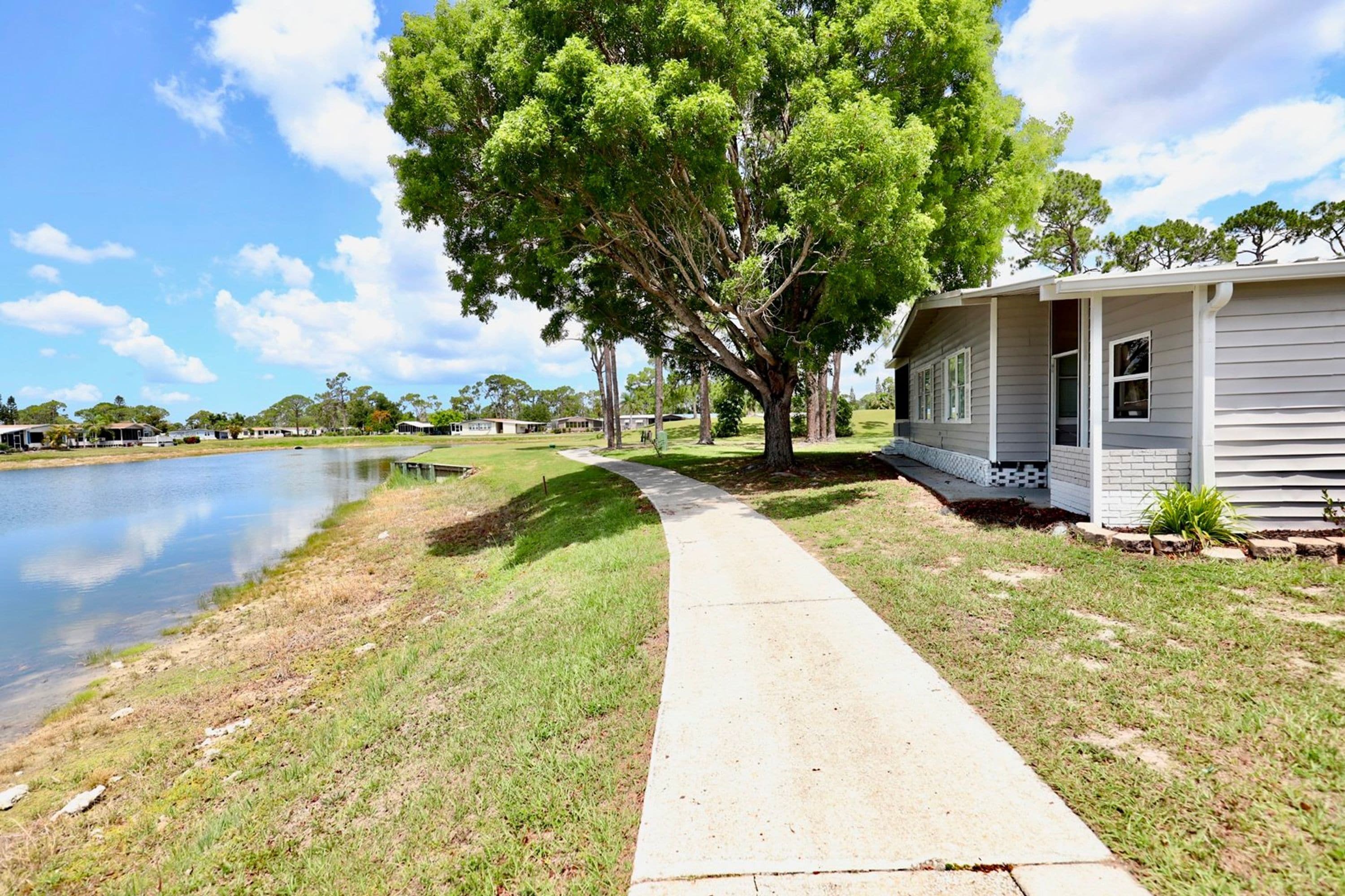 A lakeside property with a concrete pathway leading to a house with a porch.