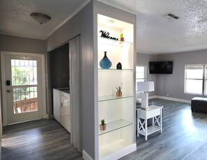 A modern living room with a glass partition, a flat-screen TV, and a white console table. - Golden Tee in North Fort Myers (North Fort Myers)