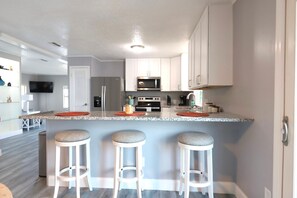 A modern kitchen with white cabinets, a granite countertop, and three bar stools. - Golden Tee in North Fort Myers (North Fort Myers)