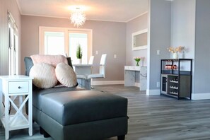 A modern living room with a grey sofa, a white side table, and a kitchen area with a marble countertop and wine rack. - Golden Tee in North Fort Myers (North Fort Myers)