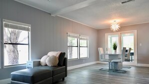 A spacious living room with a sectional sofa, a dining area with a table and chairs, large windows with blinds, and a ceiling light fixture. - Golden Tee in North Fort Myers (North Fort Myers)