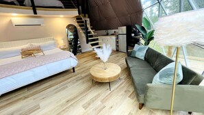 A modern interior with a wooden floor, a sofa, a round wooden coffee table, and a staircase leading to a loft area.