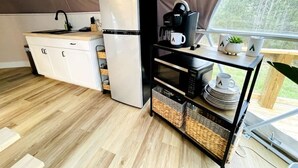 Une cuisine compacte équipée d’un réfrigérateur, d’un four à micro-ondes, d’une machine à café et d’un petit coin repas avec une table et des chaises.