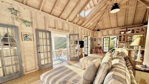 Interior acogedor de una cabaña con un sofá grande a rayas, paredes de madera y un comedor con vistas al exterior.