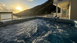 Zona de piscina con vista al mar y colinas durante el atardecer.