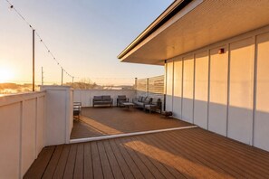 A rooftop deck with a wooden floor, outdoor seating, and string lights.