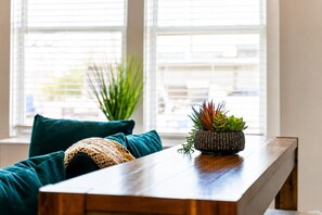 A wooden table with a woven plant pot, a teal sofa, and a woven throw blanket. - 2br home near The Nations with rooftop and views (Nashville)