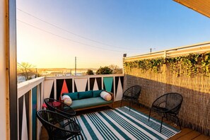 Ein Balkon mit einer Couch, zwei Stühlen, einem Streifenmuster-Teppich und einem Bambuszaun.