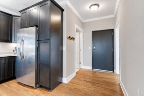A modern kitchen with dark cabinetry, a stainless steel refrigerator, and a wooden floor.