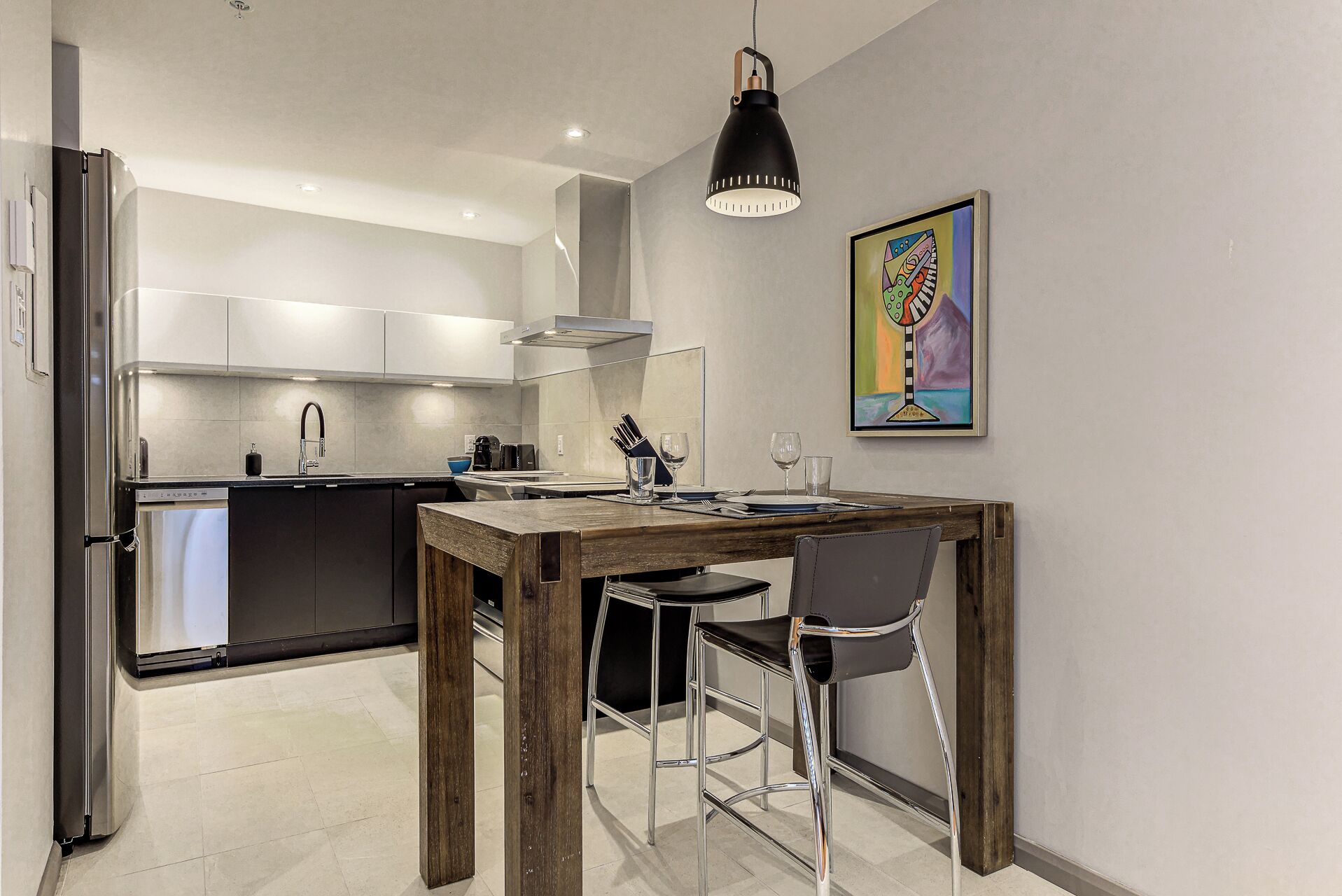 A modern kitchen with white cabinets, a stainless steel refrigerator, and a wooden dining table with two chairs.