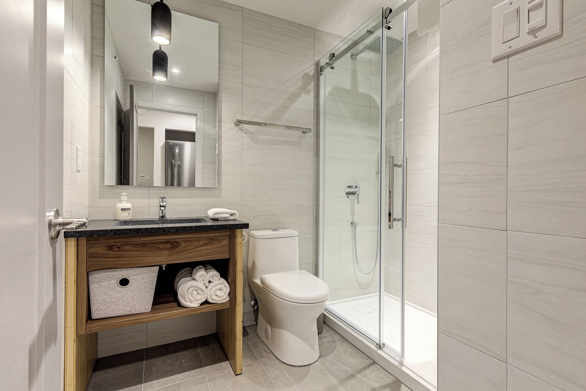 A modern bathroom with a glass-enclosed shower, a wooden vanity with a mirror, and a toilet.