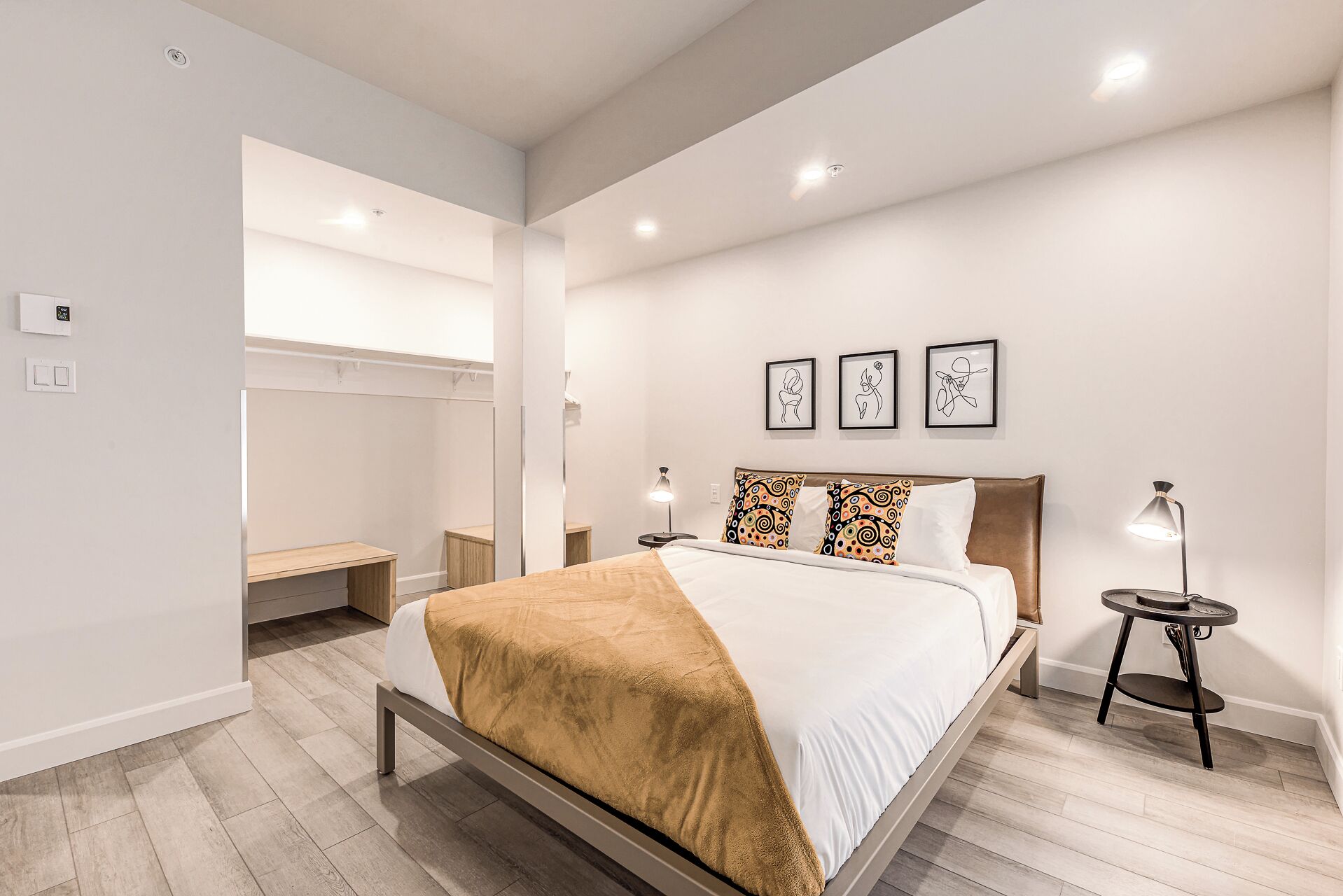 A modern bedroom with a bed, bedside tables, a bench, and wall art.