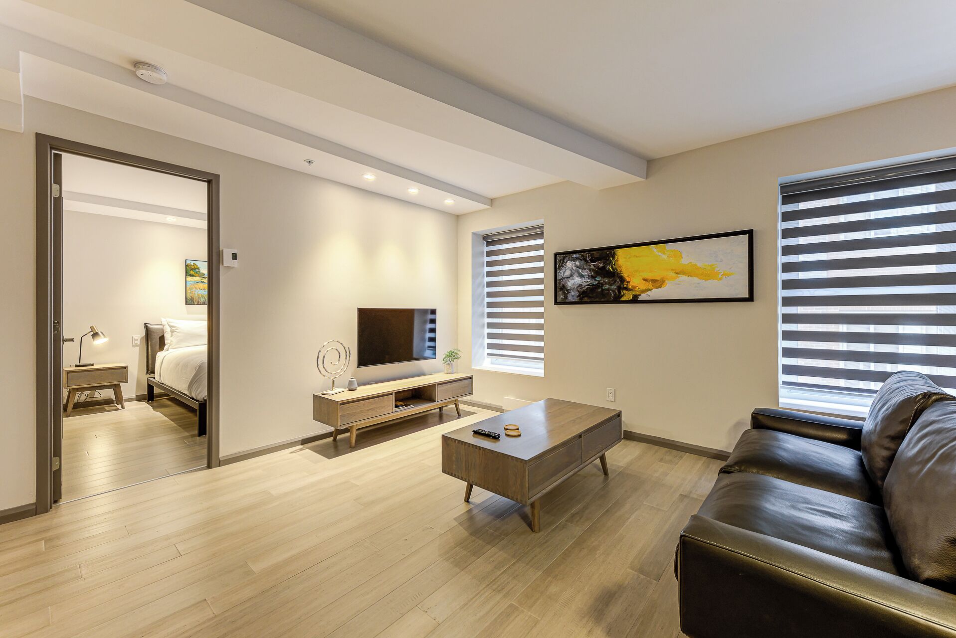 A modern living room with a wooden floor, a leather sofa, a coffee table, a TV, and a painting on the wall.