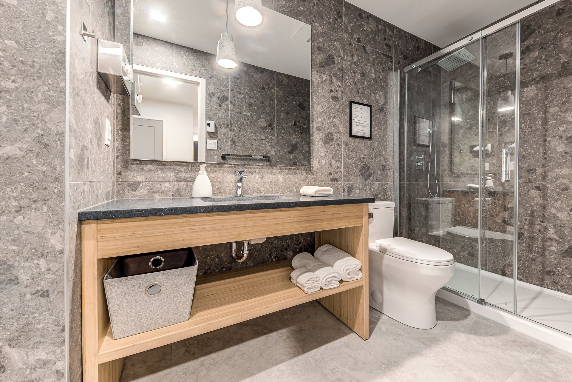 A modern bathroom with a marble backsplash, a wooden vanity, a glass shower enclosure, and a white toilet.