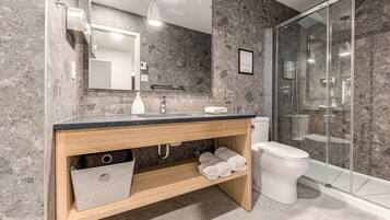 A modern bathroom with a marble backsplash, a wooden vanity, a glass shower enclosure, and a white toilet.