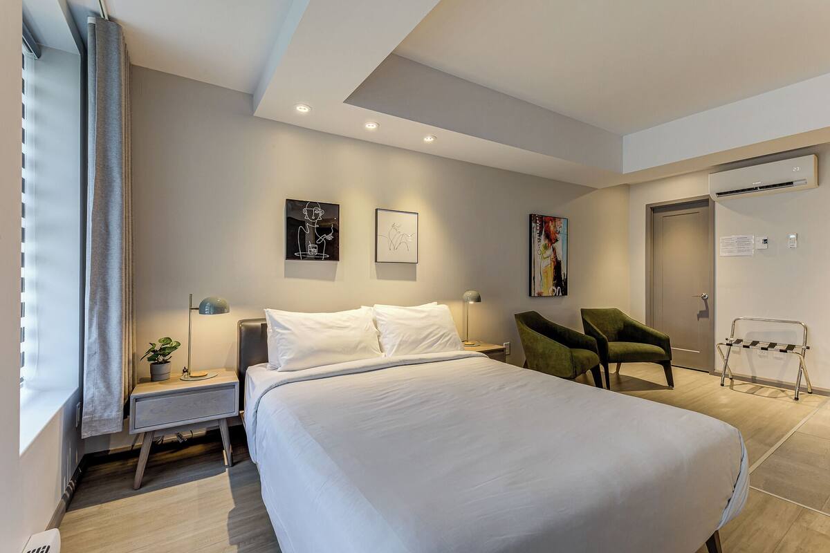 A modern hotel room with a large bed, a desk, two chairs, and artwork on the walls.
