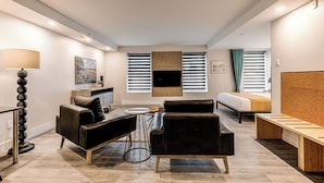 A modern living room with a sofa, a coffee table, a lamp, and a TV mounted on the wall. - 77 St-Vallier Appart Hôtel (Québec)