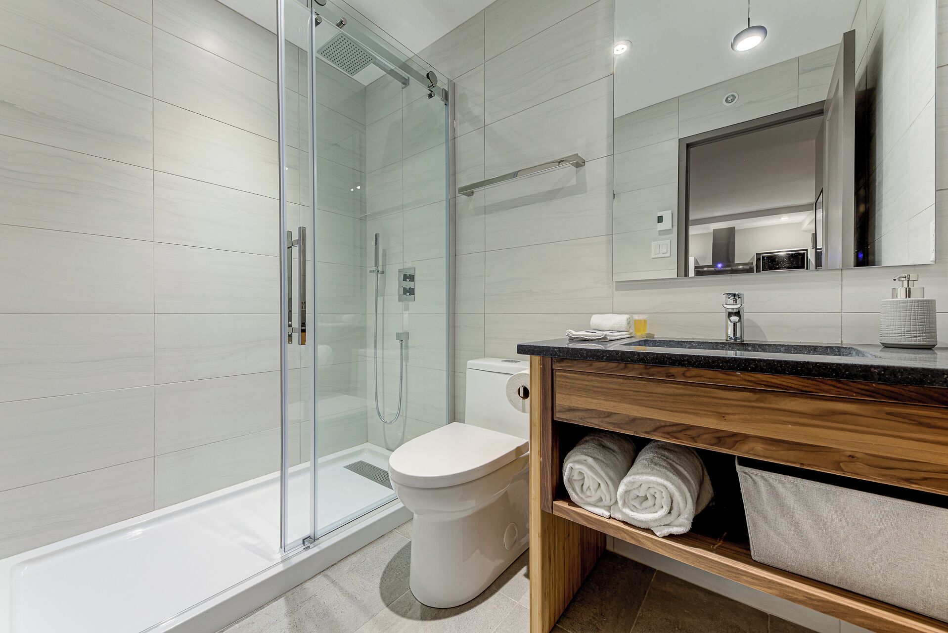 A modern bathroom with a glass-enclosed shower, a toilet, and a vanity with a mirror.