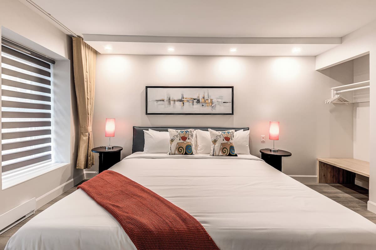 A modern hotel room with a large bed, two bedside lamps, a framed abstract painting, and a bench.