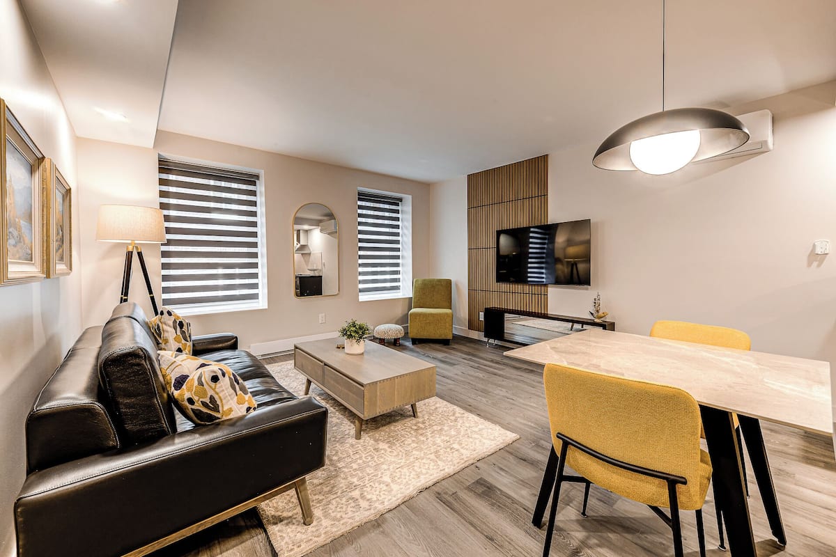 A modern living room with a sofa, coffee table, and a dining area with chairs and a TV.