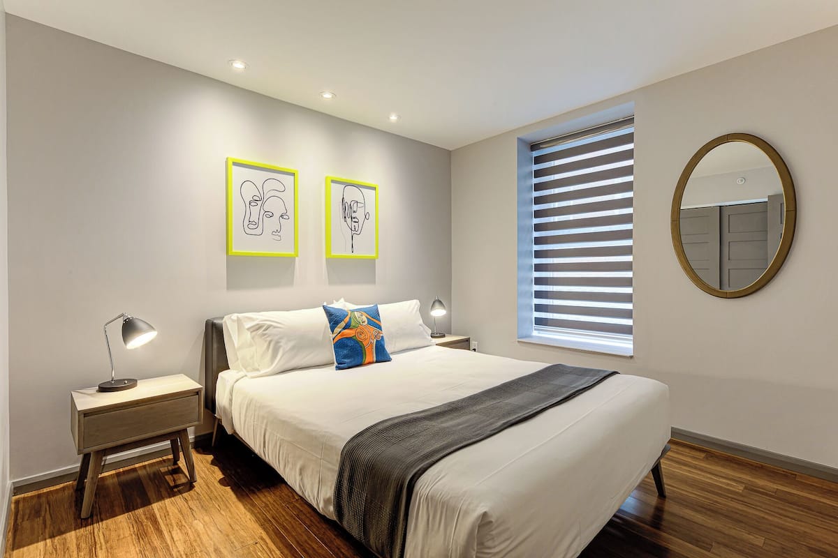 A modern bedroom with a large bed, two bedside tables, a mirror, and artwork on the wall.