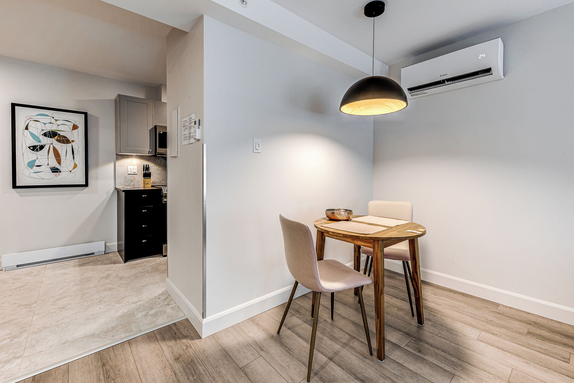 A modern kitchen with a dining area, featuring a wooden table and chairs, a pendant light, and an air conditioning unit.