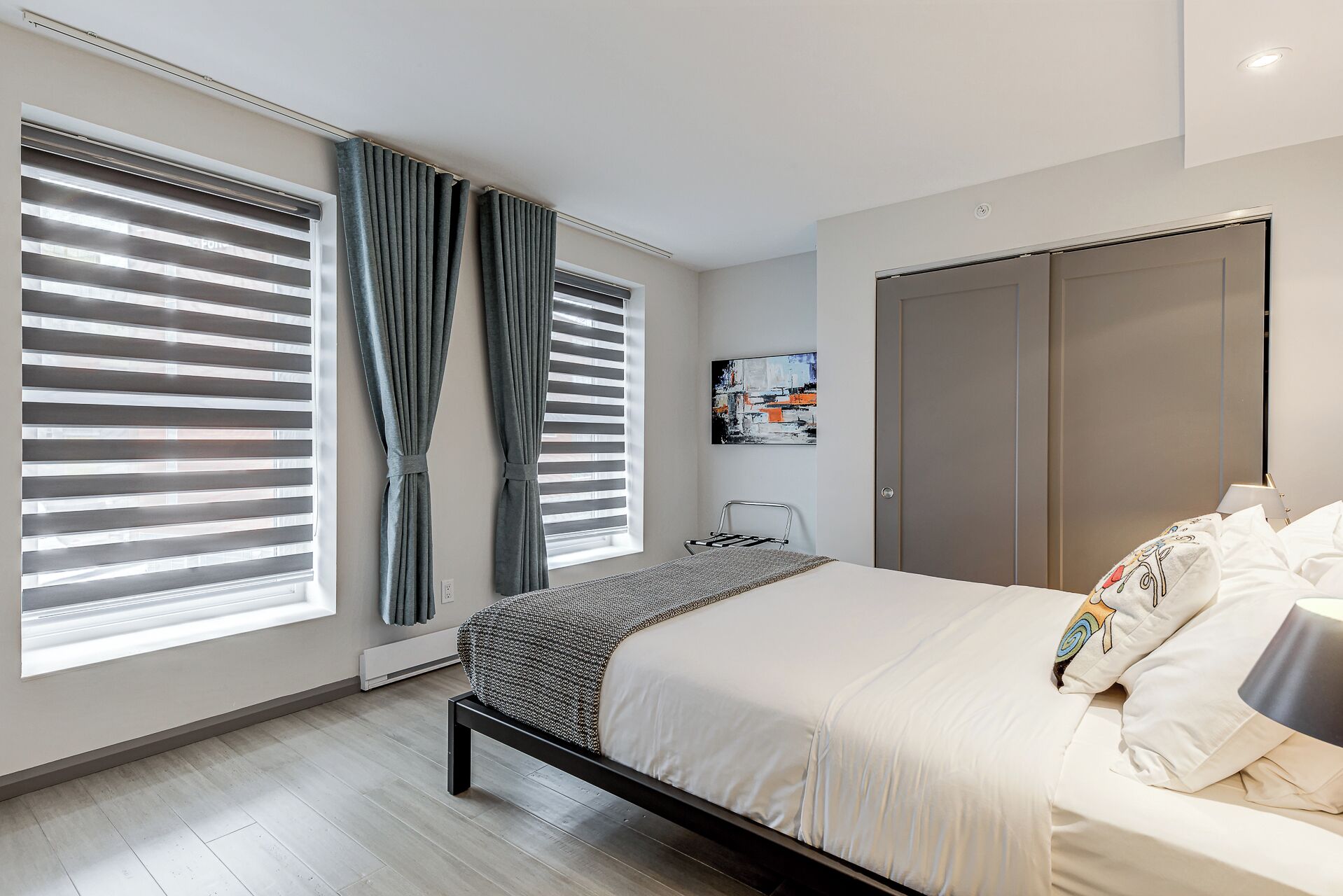 A modern bedroom with a bed, curtains, a radiator, a painting, and a wardrobe.