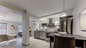 A modern kitchen with a central island, stainless steel appliances, and a dining area with a chair. - 77 St-Vallier Appart Hôtel (Québec)