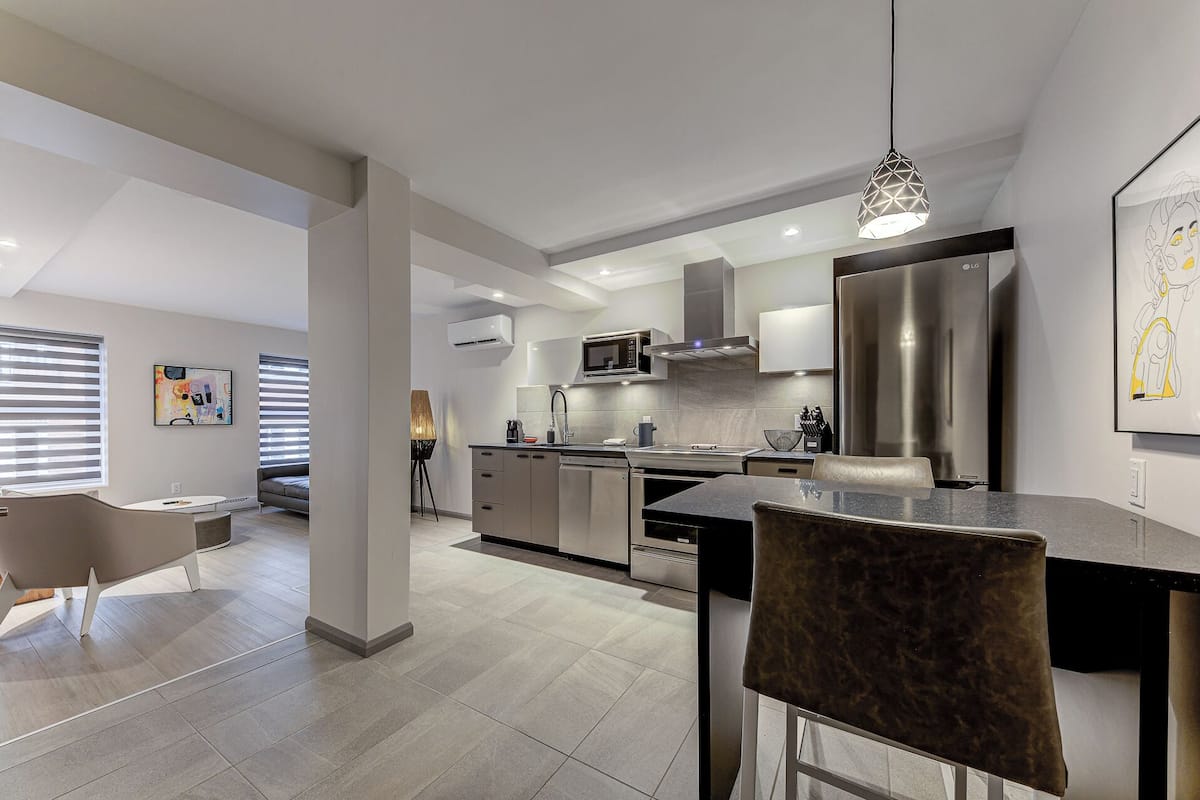 A modern kitchen with a central island, stainless steel appliances, and a dining area with a chair.