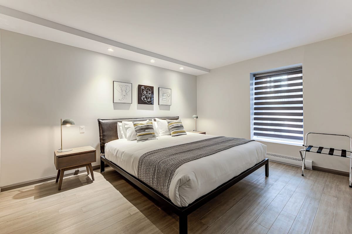 A modern bedroom with a large bed, bedside tables, a standing lamp, and a window with blinds.