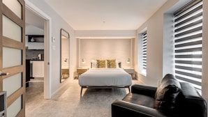 A modern bedroom with a large bed, a black leather chair, and a walk-in closet. - 77 St-Vallier Appart Hôtel (Québec)