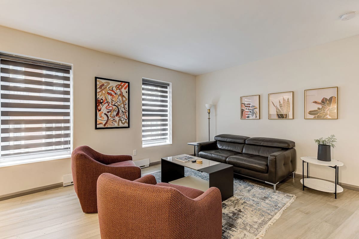 A modern living room with a leather sofa, two armchairs, a coffee table, and artwork on the walls.