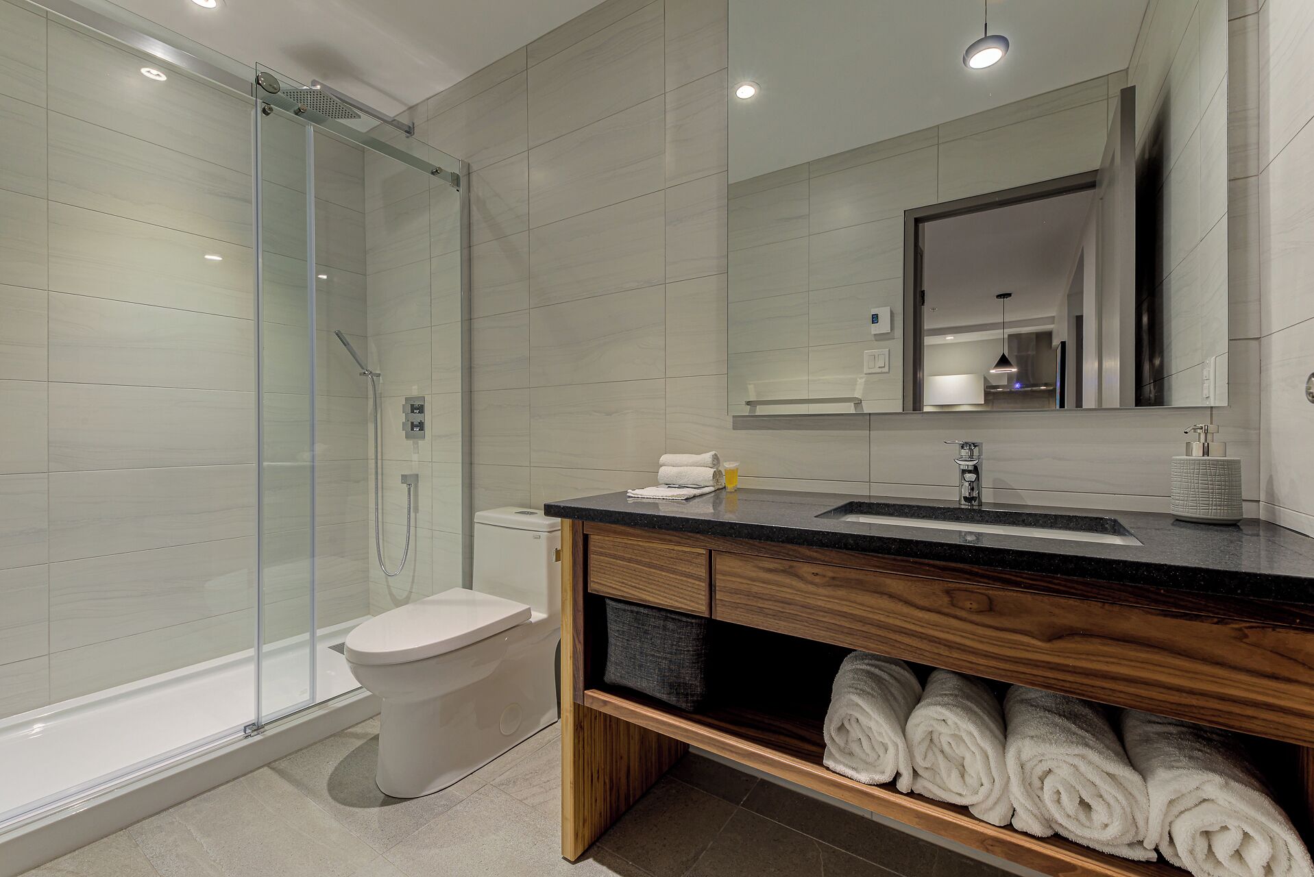 A modern bathroom with a glass shower enclosure, a white toilet, a wooden vanity with a sink, and a mirror.